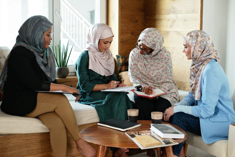 Four Muslim women in hijabs collaborating in a modern indoor office space, discussing ideas together.